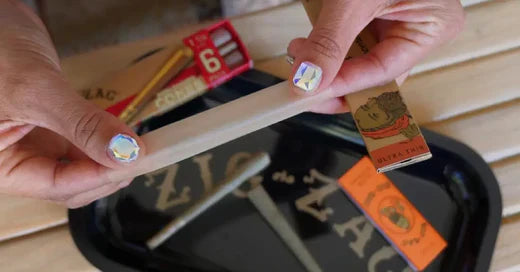 Zig-Zag ultra-thin rolling papers being held by a person with holographic nail art over a branded tray