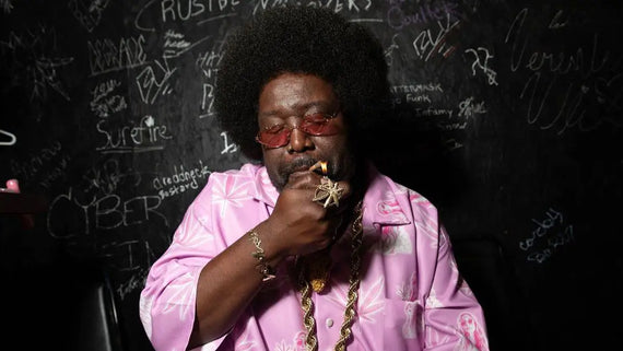 Slow-burning rolling paper being lit by a man in a pink patterned shirt against a chalkboard wall