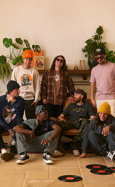Group of friends wearing Zig-Zag branded apparel, gathered in a cozy living room with plants and vinyl records.