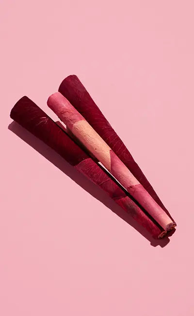Rose cone rolling paper in shades of pink and red, elegantly arranged on a soft pink background.