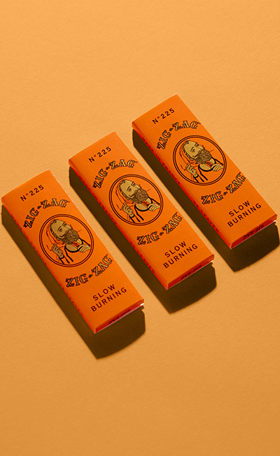 Hemp paper Zig-Zag rolling papers in bright orange packaging with a vintage logo, arranged on a warm-toned background.