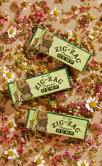 Zig-Zag organic hemp rolling papers displayed on a bed of dried chamomile and pink flowers.