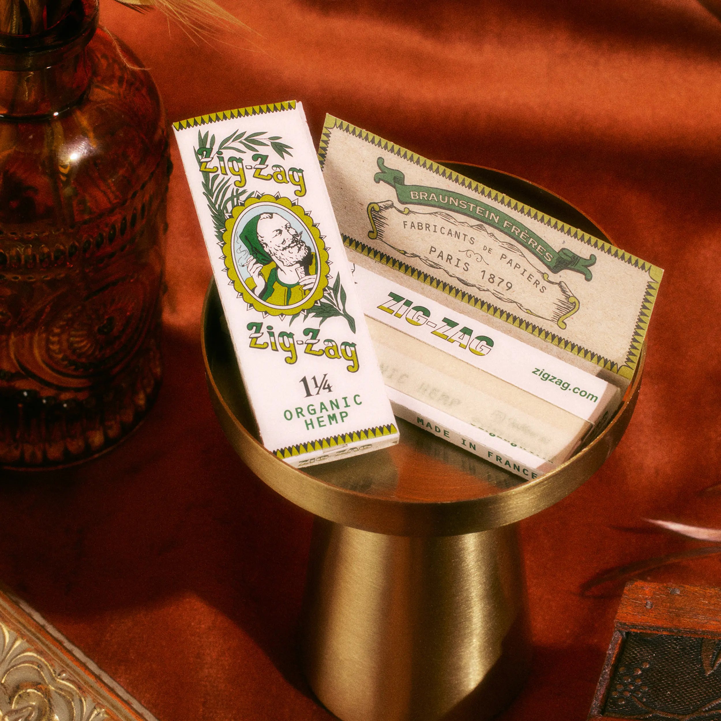 Zig-Zag 1 1/4 Organic Hemp rolling papers displayed on a gold stand with warm, decorative surroundings.