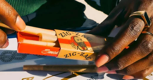 Zig-Zag pre-rolled cones being taken out of a red and gold branded package by a person with gold rings