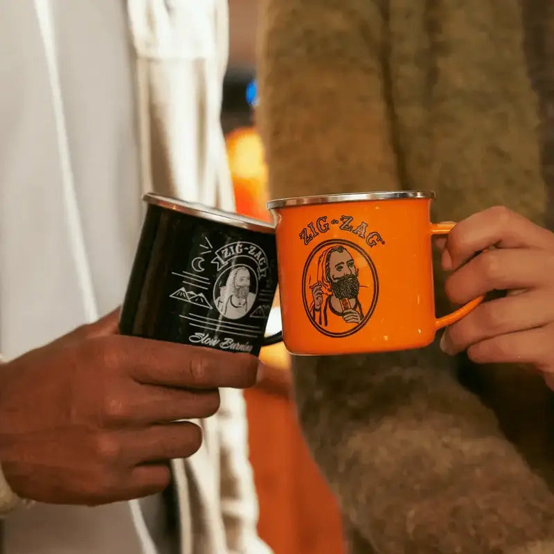 Two people holding Zig-Zag branded mugs, one black and one orange, in a casual indoor setting