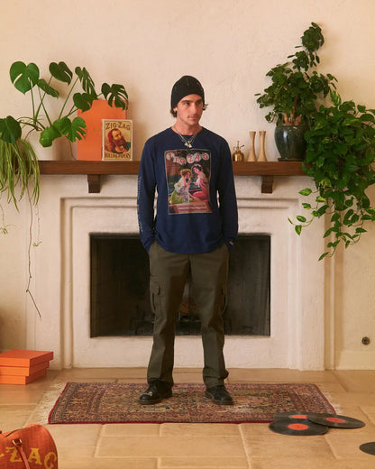 Long sleeve Zig-Zag shirt with vintage artwork on the front, worn casually in a warm, plant-filled room.