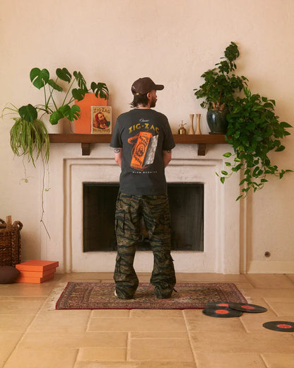Zig-Zag t-shirt featuring a large orange pack graphic on the back, worn casually in a cozy living room setting.
