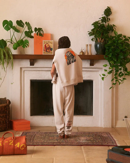 Zig-Zag cream sweatpants with logo on the leg, styled with matching top draped over shoulders.