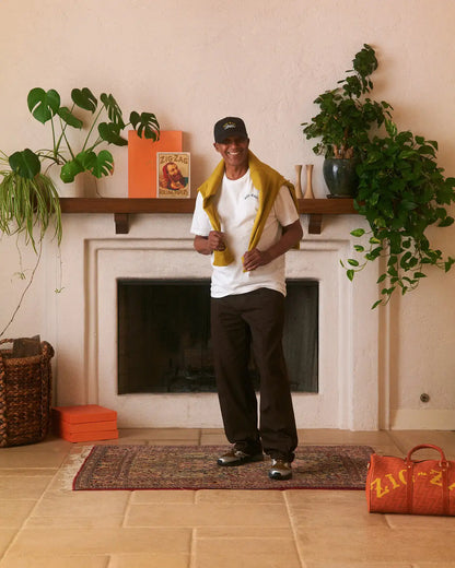 Zig-Zag t-shirt in white with small chest logo, styled casually with a yellow sweater and black pants.