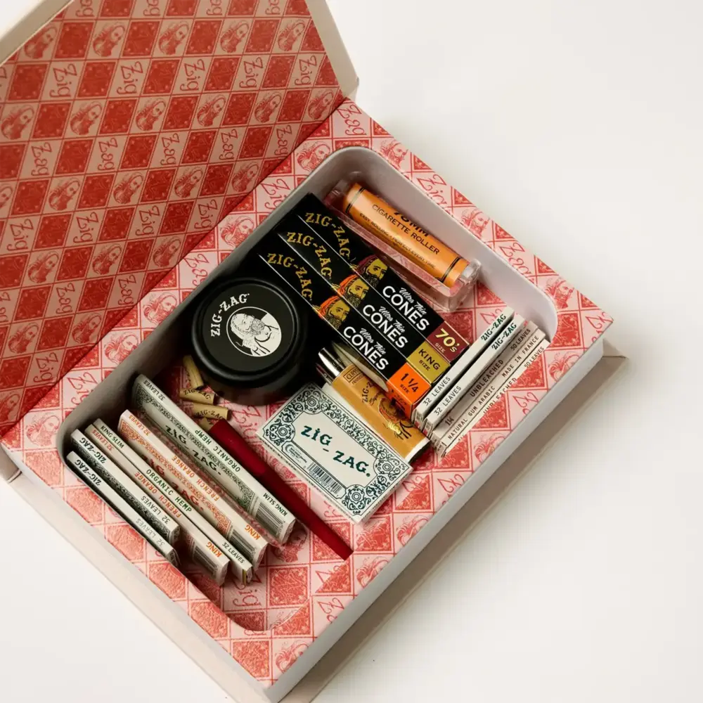 Zig-Zag stash box containing rolling papers, pre-rolled cones, a grinder, and other smoking accessories neatly organized.